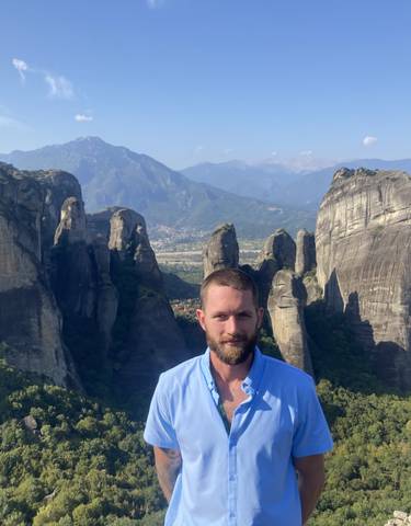 Man standing in front of towering rocky formations with scenic mountains.