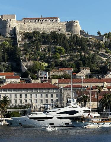 A picturesque view of a yacht in front of historic buildings and a fort on Hvar Island, Croatia.