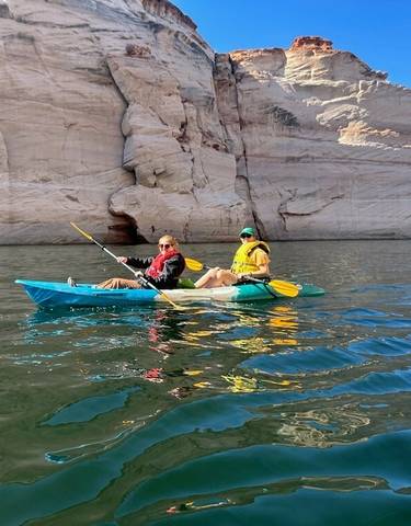 Two people kayaking on a clear blue lake surrounded by rocky cliffs.