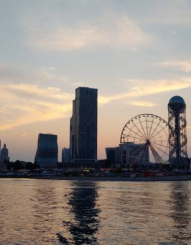 City skyline at sunset with a ferris wheel and tall buildings.