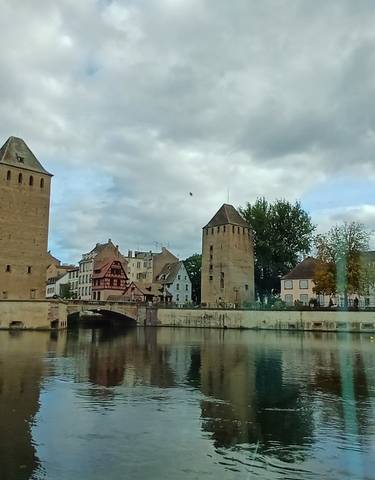 Historic buildings by a river under a cloudy sky.