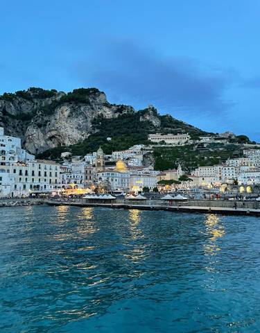 Amalfi Coastline with buildings nestled into a hill by the sea at dusk.
