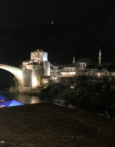 Mostar Bridge lit up at night over a river.