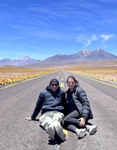 Two people sitting on a road with mountains in the background.