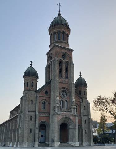 A brick cathedral with multiple domes and a spire under clear sky.