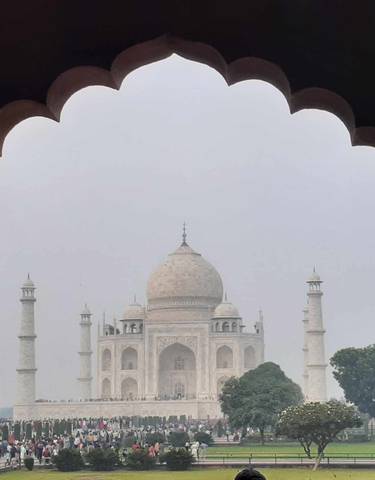 Taj Mahal viewed through an ornate archway on a hazy day.