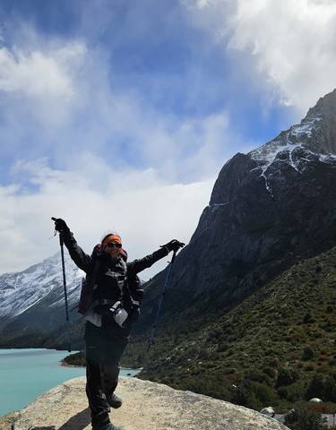 Hiker posing with trekking poles in front of snow-capped mountains.
