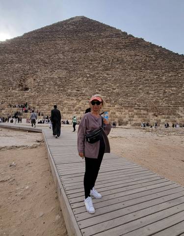Woman posing in front of a pyramid with many visitors.