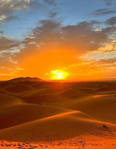 Sunset over sand dunes with a dramatic sky.