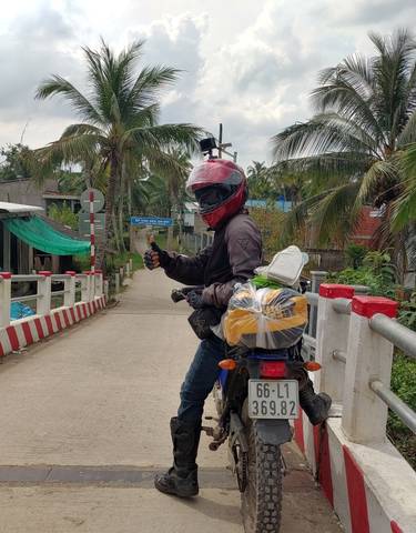Motorcyclist on a bridge in a rural area with palm trees.