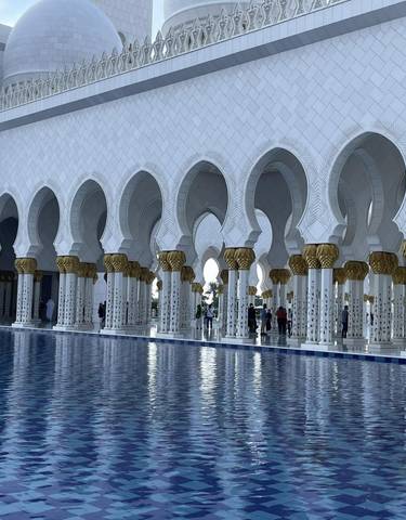 Tourists at a mosque with arches and water in front.