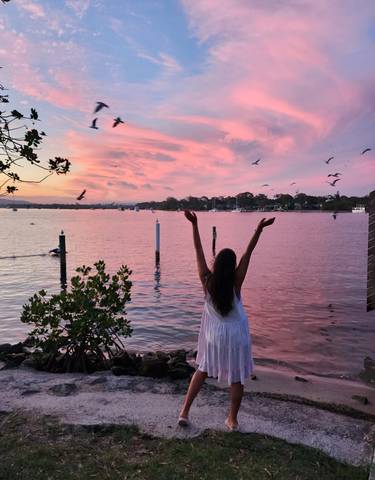 Woman with arms raised embracing a picturesque pink sunset by the water.