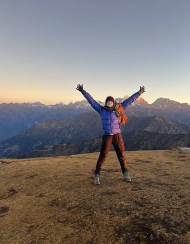 Person with arms raised on a mountain top at sunrise.