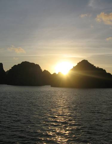 Sunset over the ocean with rocky silhouettes on the horizon.
