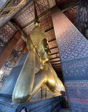 Golden Buddha statue indoors with intricate patterns on the wall.
