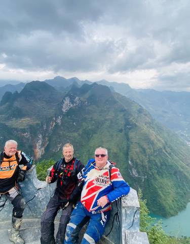 Three people in motorcycle gear posing with dramatic mountain scenery.