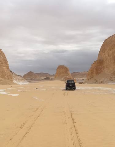 A car driving between large desert rock formations.