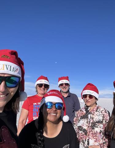 A group of people wearing Bolivia Santa hats smiling for a photo on a salt flat.