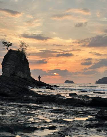 Person standing on a rock during a dramatic sunset over the ocean.