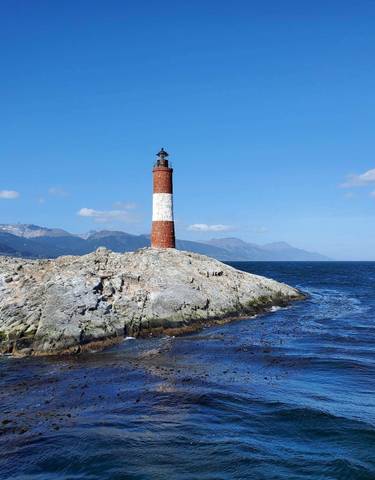 Lighthouse on a rocky shore with a mountainous backdrop.