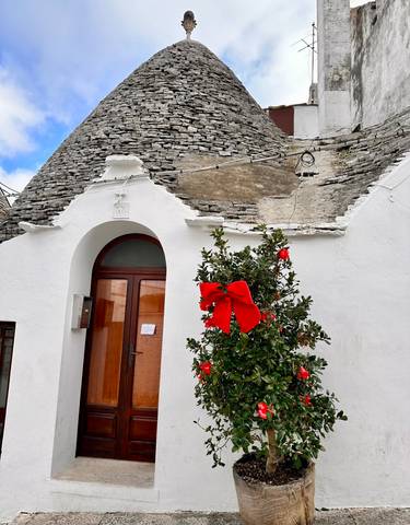 Traditional white conical building, possibly a trullo, decorated with a red bow.