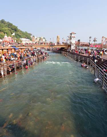 Crowded riverside bathing area with people.