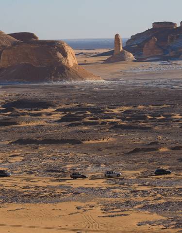 Dramatic desert landscape with vehicles on a journey.