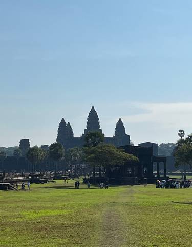 View of Angkor Wat with grass and trees in the foreground.