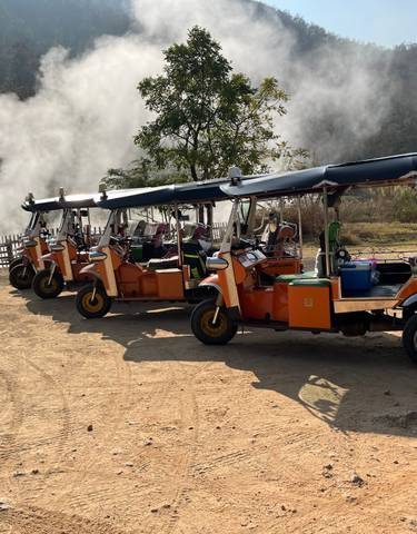 Row of tuk-tuks parked with steam rising in the background.