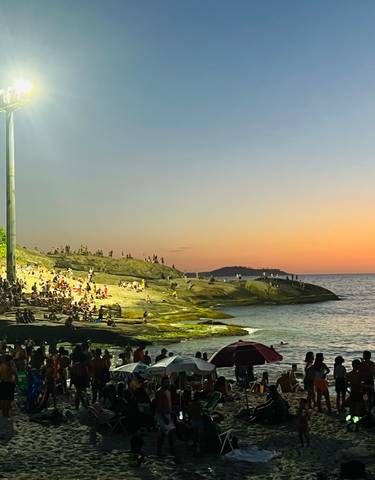 Crowded beach at sunset, people enjoying the view.