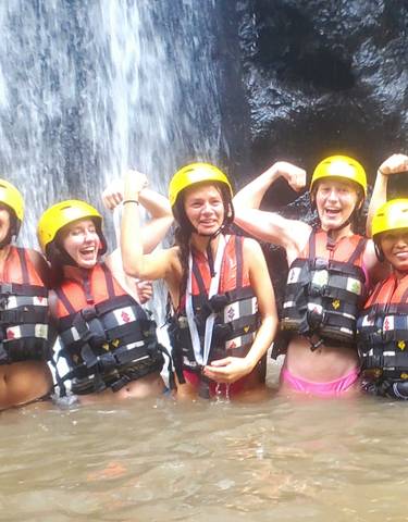 Group of women posing in a waterfall pool wearing helmets.