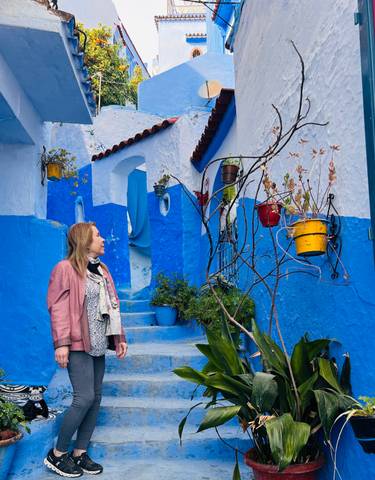 Person in a blue alley with colorful flower pots.