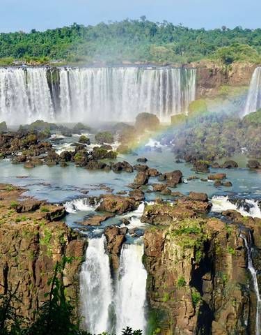 Grand waterfall with rainbow over lush forest.