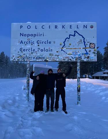 Three people at the Arctic Circle sign.
