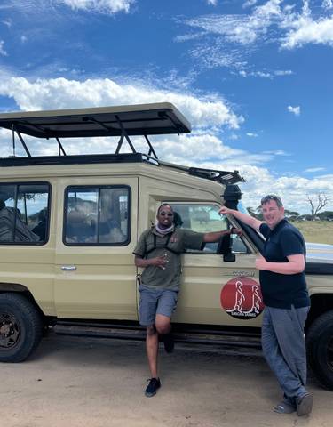 Two men posing with a safari vehicle under a blue sky.