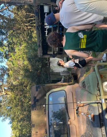 People exploring an outdoor area with military vehicles.