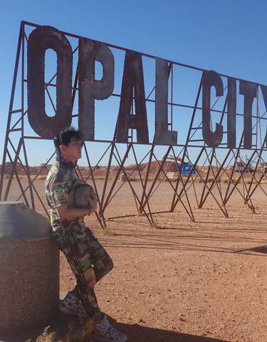 Person leaning against a large metallic sign in a desert.