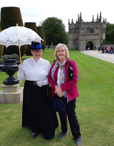 Two women pose in historical costumes in front of an old stone building