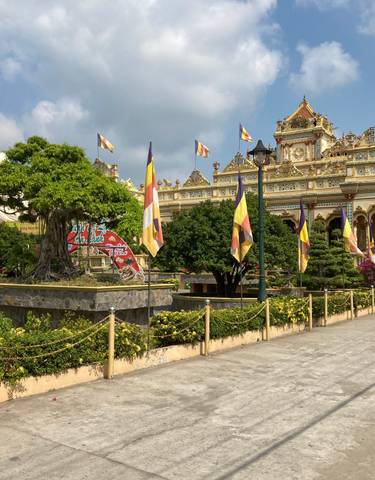 A vibrant temple with flags, plants, and visitors.