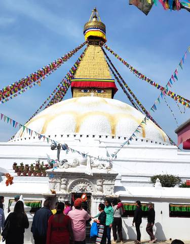 Large white stupa with prayer flags and eyes painted on it.
