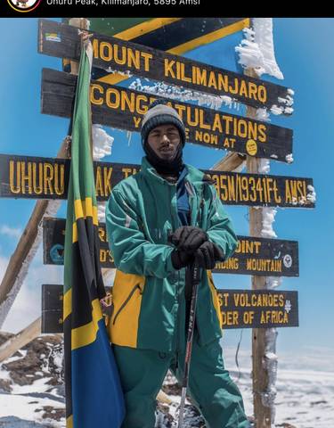 Person standing at Uhuru Peak signpost with snow in the background.