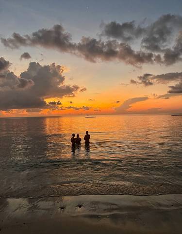 Two people in shallow ocean water during a vibrant sunset.