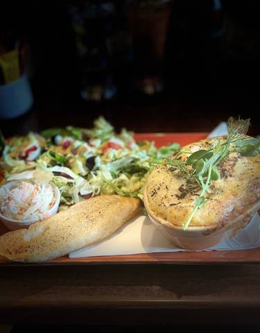 A meal consisting of a pie, salad, and bread on a wooden table.