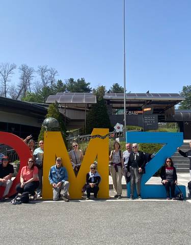 Tour group posing with large colorful letters spelling 'DMZ'.