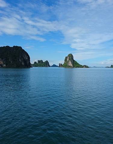 Vast scenery of a bay with limestone islands under a bright blue sky.