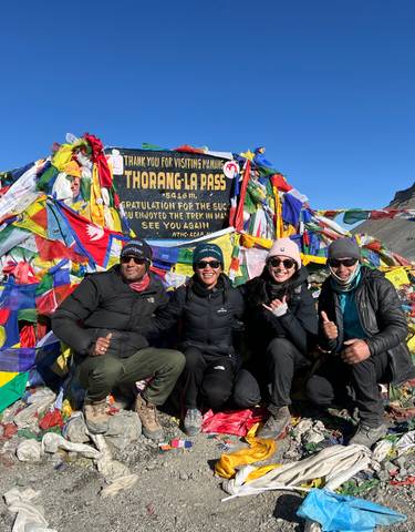 Group of trekkers posing at Thorong La pass, surrounded by flags.