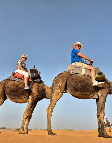 Two people riding camels in a desert landscape.