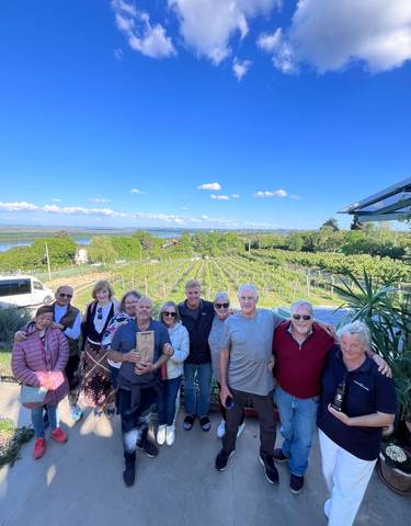 Group posing in front of a vineyard with blue skies.