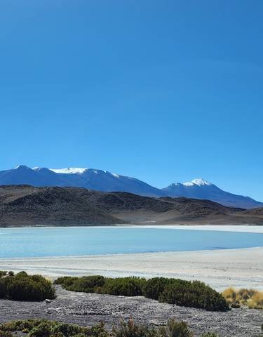 Turquoise lagoon with mountains in the background under a clear sky.