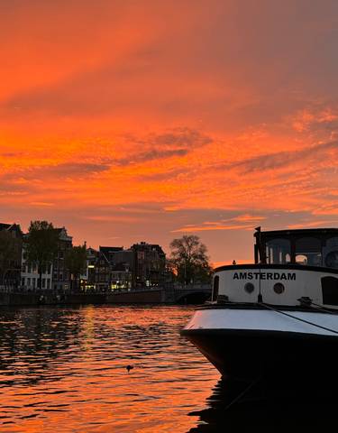 Boat docked at a canal during a stunning orange sunset.